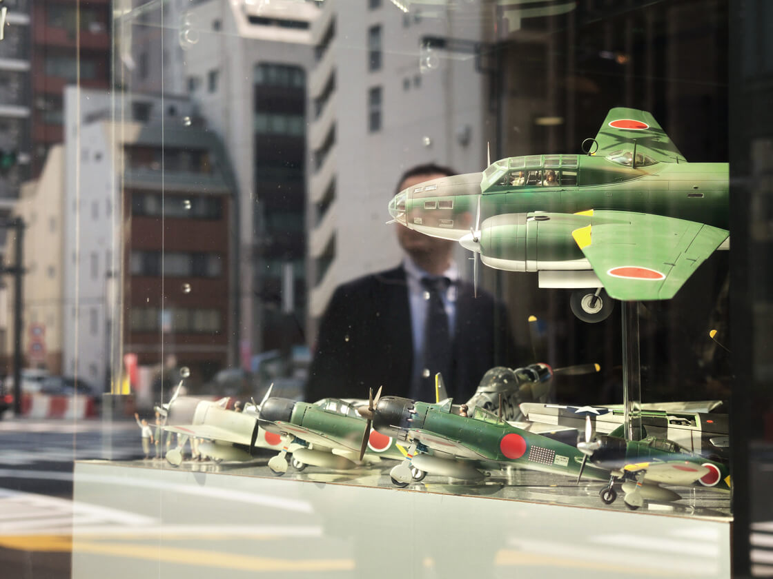 the reflection of a salaryman in a shop selling WW2 plane scale models in Shimbashi